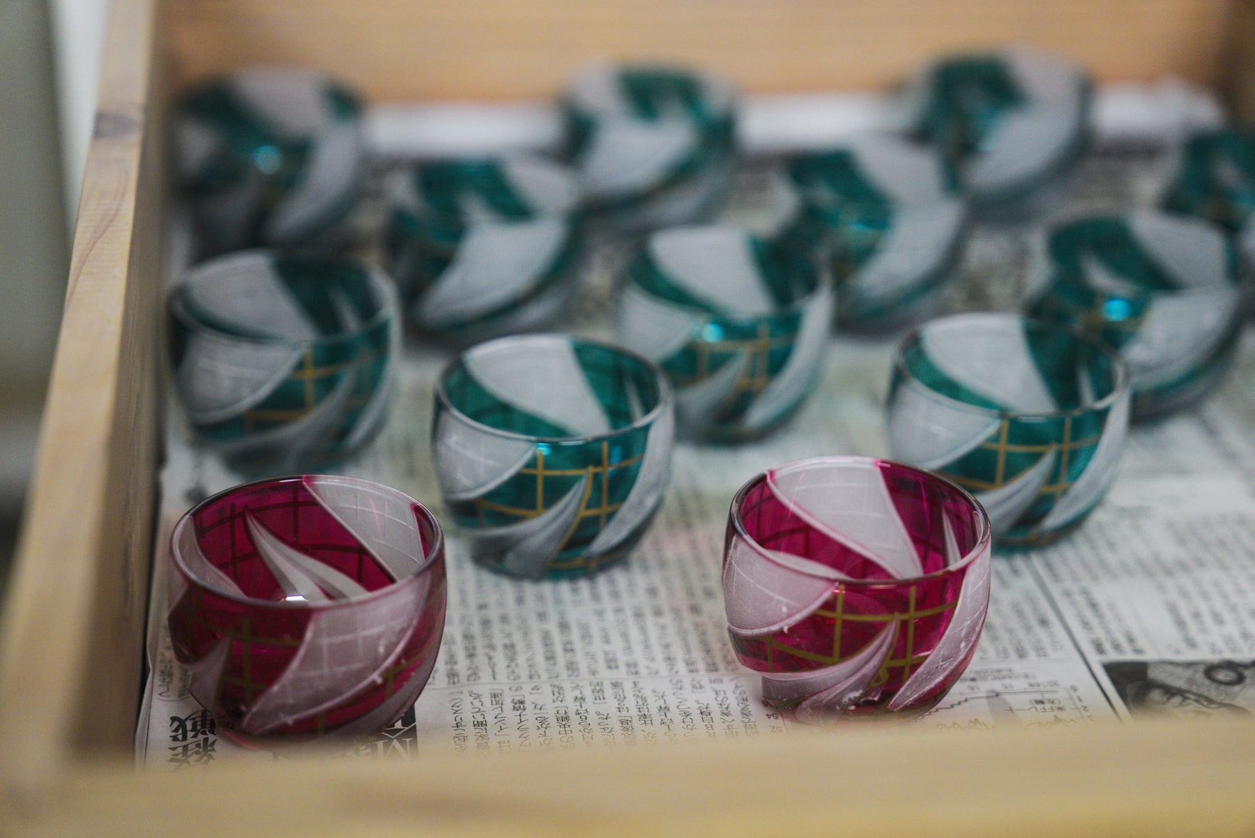 Teal and cranberry cut-glass cups with a bold swirl pattern, packed in a crate