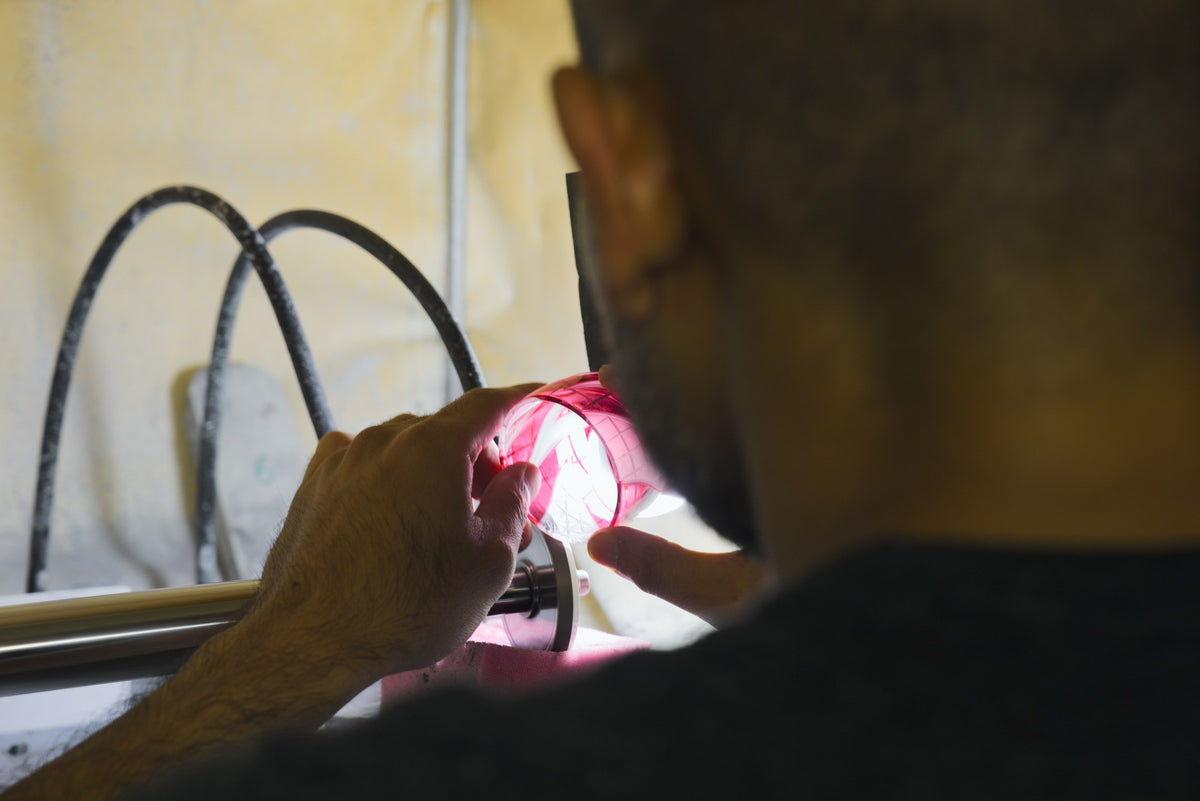 Craftsman checking a red cut-glass piece against a lamp