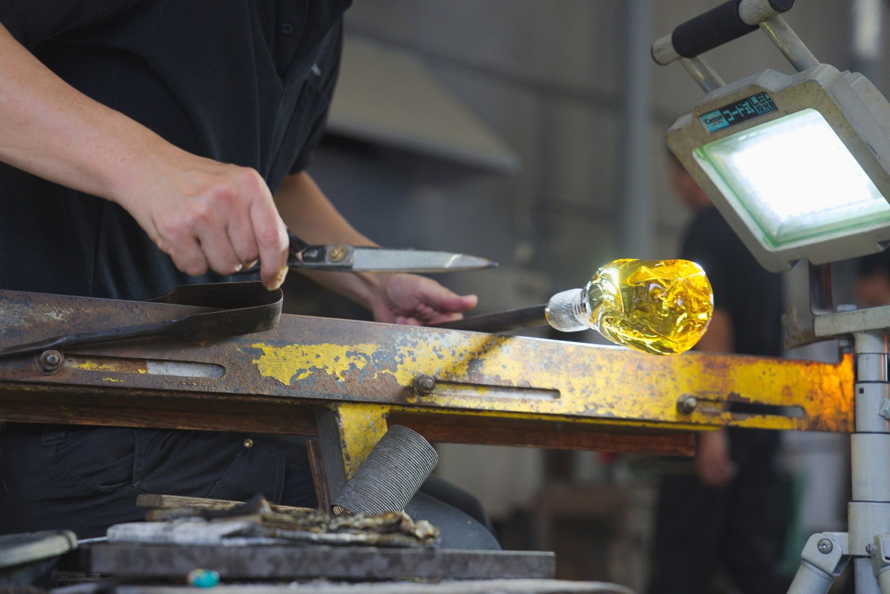 Hands shaping a glowing amber glass blank with shears