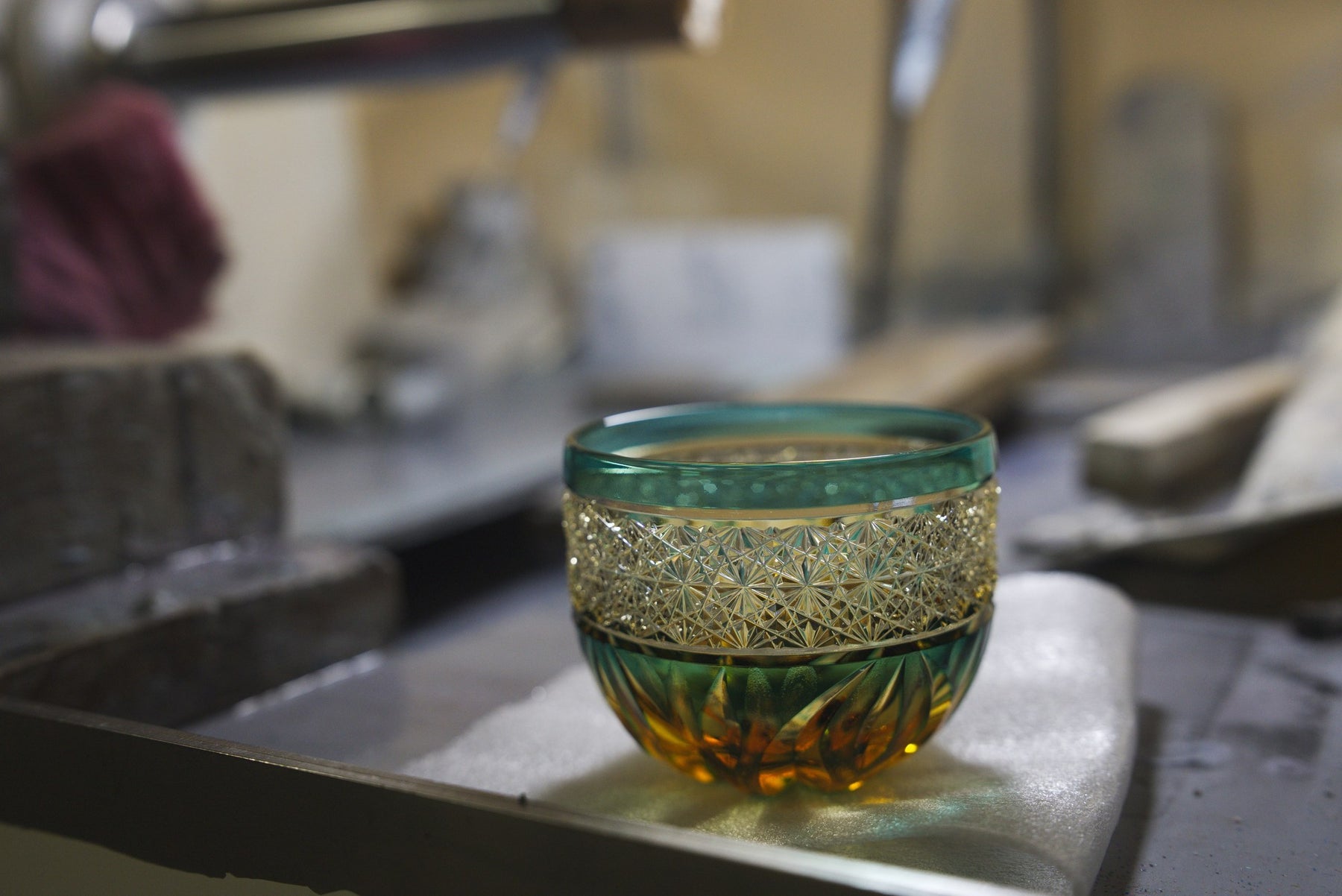 Cut-glass cup with a dense faceted band, resting at the cutting-wheel station